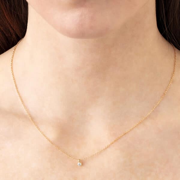 A woman wearing a gold necklace with a small diamond.