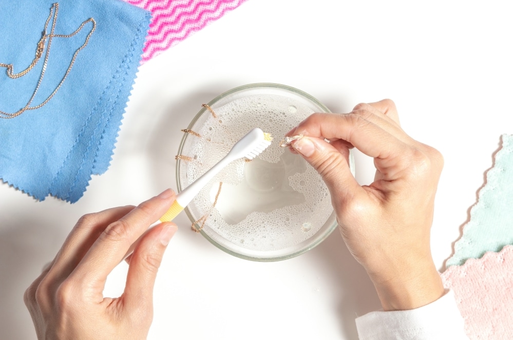 Woman cleaning fine jewelry using a toothbrush and soapy water